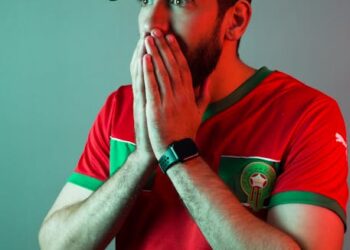 A dynamic and vibrant image capturing the essence of Moroccan football, featuring the national team's 'Lions of the Atlas' emblem, a stadium filled with passionate fans holding Moroccan flags, and subtle architectural elements of Morocco in the background. The mood should be celebratory and full of national pride.
