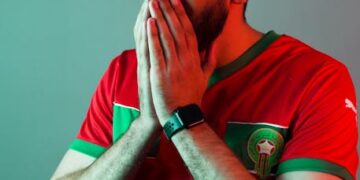 A dynamic and vibrant image capturing the essence of Moroccan football, featuring the national team's 'Lions of the Atlas' emblem, a stadium filled with passionate fans holding Moroccan flags, and subtle architectural elements of Morocco in the background. The mood should be celebratory and full of national pride.